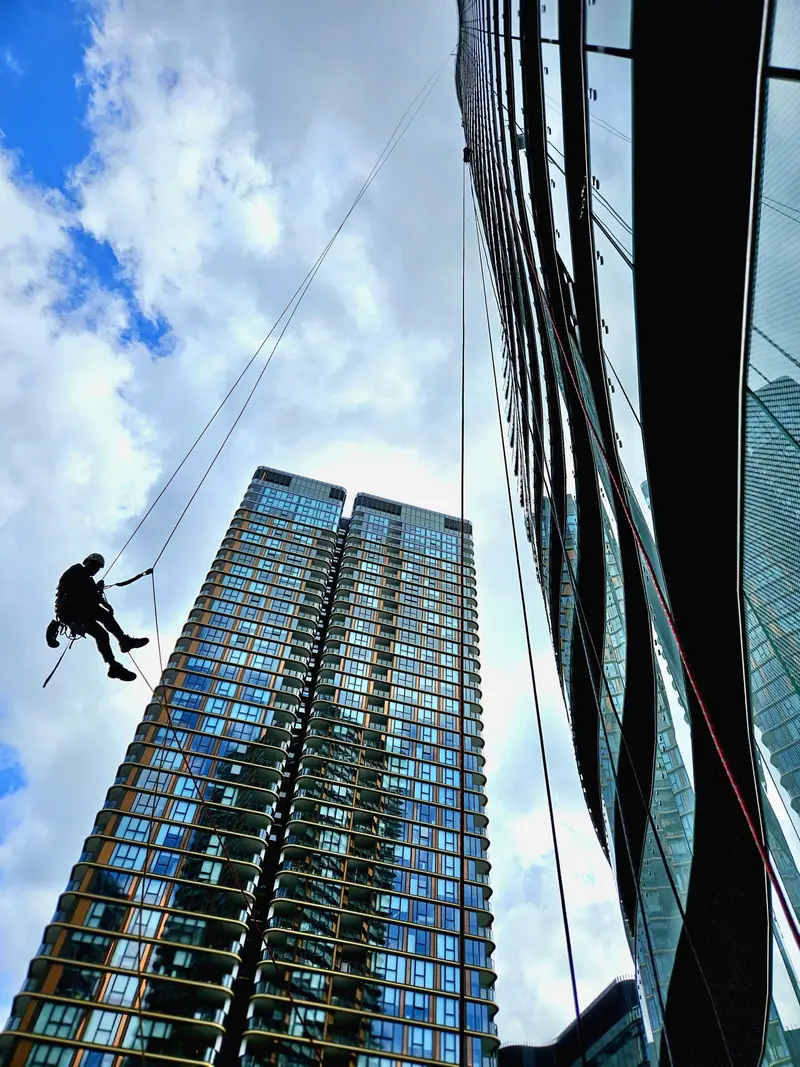Technician on ropes beside a glass residential tower